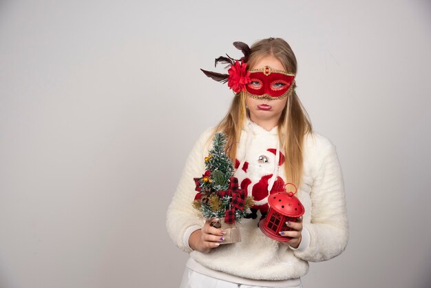 Vrouw in maskerademasker met cadeau en dennenboom.