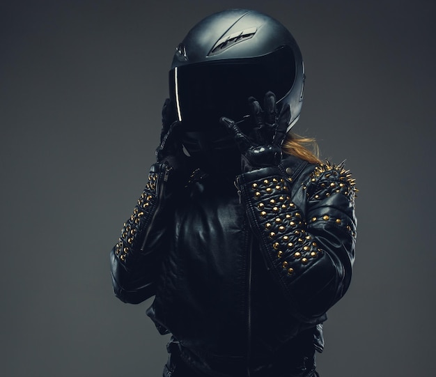 Vrouw in motorhelm en lederen kleding geïsoleerd op een grijze achtergrond in de studio.