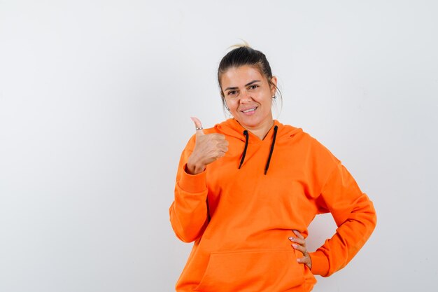 Vrouw in oranje hoodie die duim opsteekt en er gelukkig uitziet