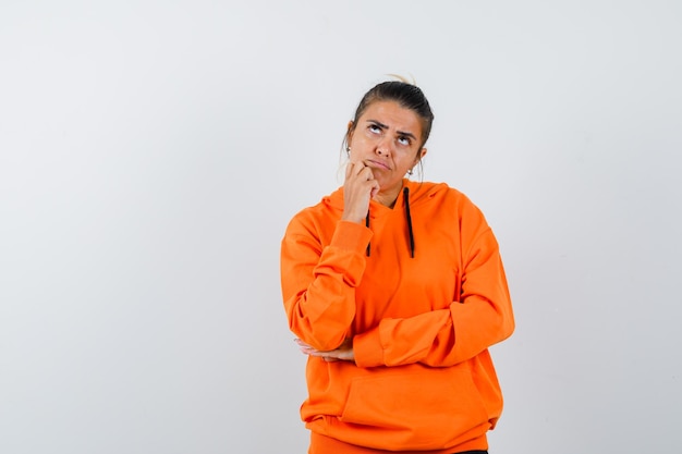 Vrouw in oranje hoodie die haar kin steunt en aarzelend kijkt