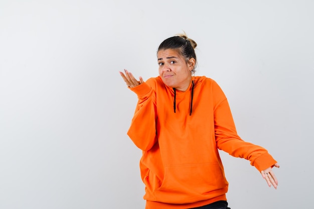 Vrouw in oranje hoodie die hulpeloos gebaar toont en verward kijkt