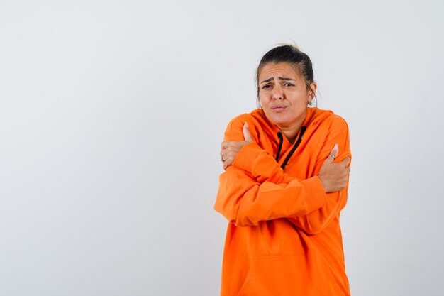 Vrouw in oranje hoodie die zichzelf omhelst of het koud heeft en er hulpeloos uitziet