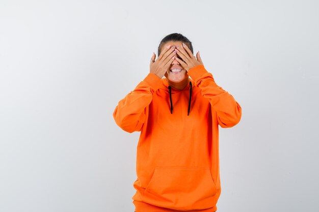 Vrouw in oranje hoodie houdt handen op ogen en kijkt opgewonden