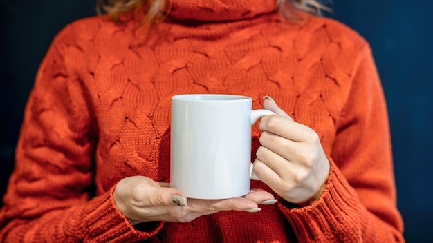 Vrouw in oranje trui met een witte beker met beide handen,