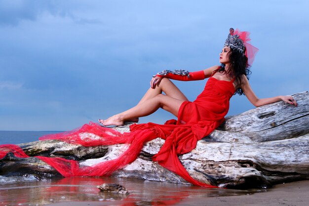Vrouw in rode avantgarde jurk op het strand
