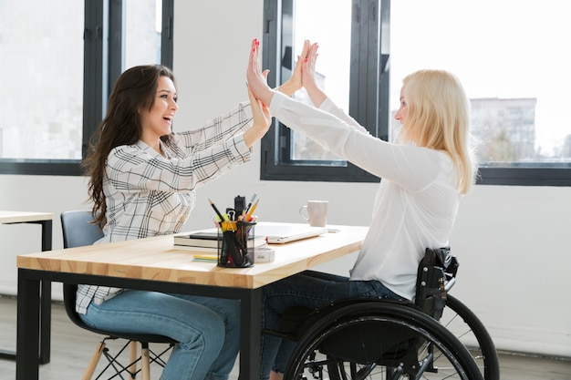 Vrouw in rolstoel high-fiving met haar collega