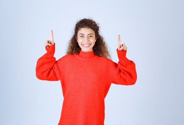 vrouw in rood shirt wijzend naar iemand of ergens met een emotioneel gezicht op blauw.