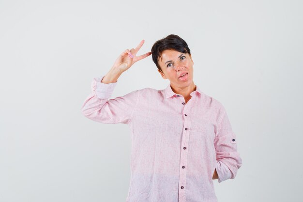 Vrouw in roze shirt met overwinning gebaar en op zoek naar zelfverzekerd, vooraanzicht.