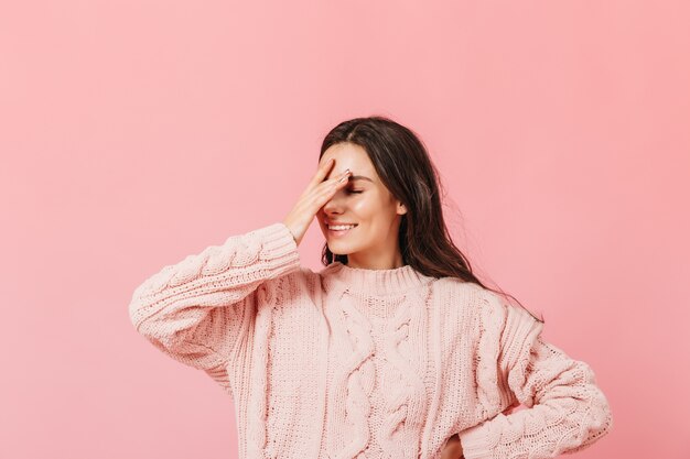 Vrouw in roze trui poseren op geïsoleerde achtergrond. Grappig meisje met glimlach maakt facepalm.