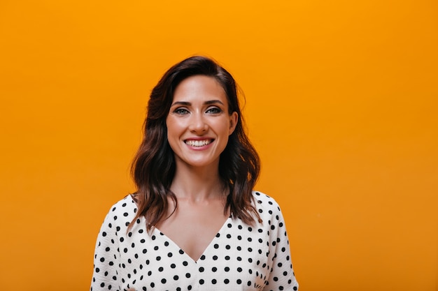 Vrouw in schattige blouse lacht op oranje achtergrond