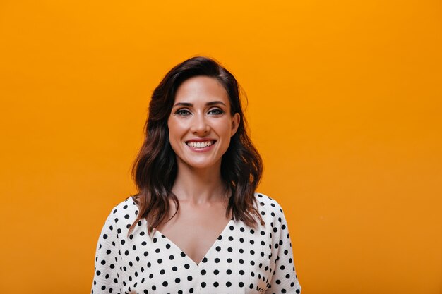 Vrouw in schattige blouse lacht op oranje achtergrond
