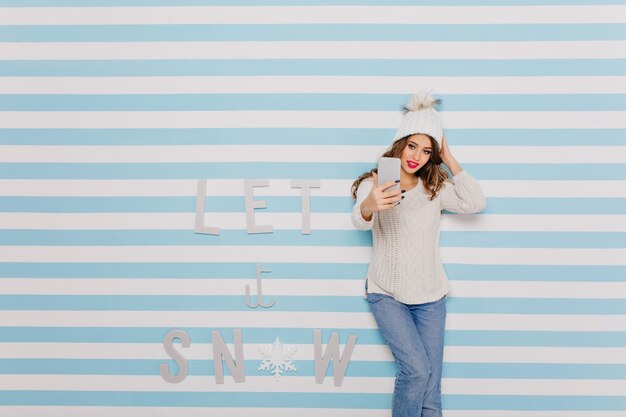 Vrouw in spijkerbroek selfie te nemen naast winter inscriptie: laat het sneeuwen