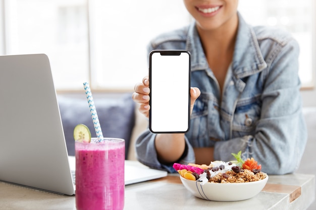 Vrouw in stijlvol denim jasje in coffeeshop met leeg smartphonescherm