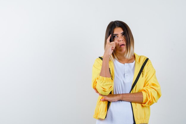 Vrouw in t-shirt, jasje dat de vinger op de slapen houdt en peinzend kijkt, vooraanzicht.