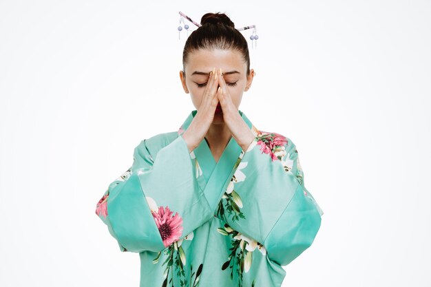 Gratis foto vrouw in traditionele japanse kimono die er droevig uitziet en hads bij elkaar houdt op wit?