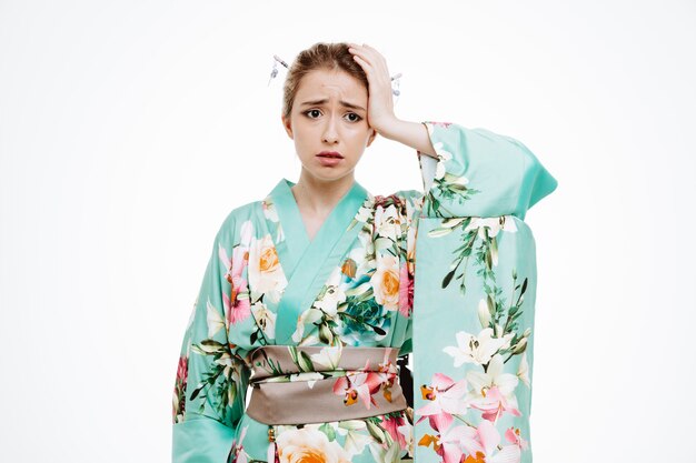 Vrouw in traditionele Japanse kimono die er verward en bezorgd uitziet en hand op haar hoofd houdt voor een fout op wit