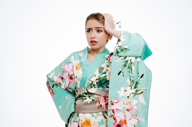 Vrouw in traditionele Japanse kimono kijkt verward en bezorgd opzij terwijl ze de hand op haar hoofd houdt voor een fout op wit