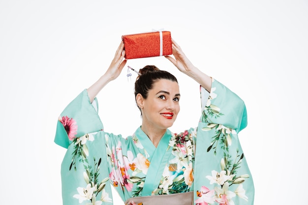 Vrouw in traditionele japanse kimono met een cadeautje op haar hoofd, blij en blij op wit