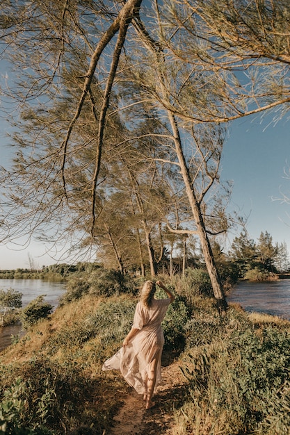 Gratis foto vrouw in witte jurk lopen op blote voeten in een klein grasveld omringd door water