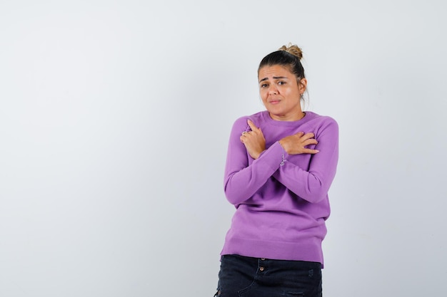 Vrouw in wollen blouse met gekruiste handen op de borst en hulpeloos kijkend