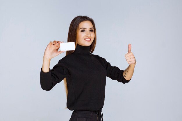 vrouw in zwart shirt toont haar visitekaartje en ziet er tevreden uit.