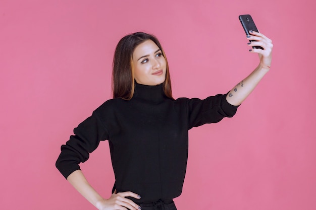 Vrouw in zwarte trui met een smartphone en haar selfie te nemen.