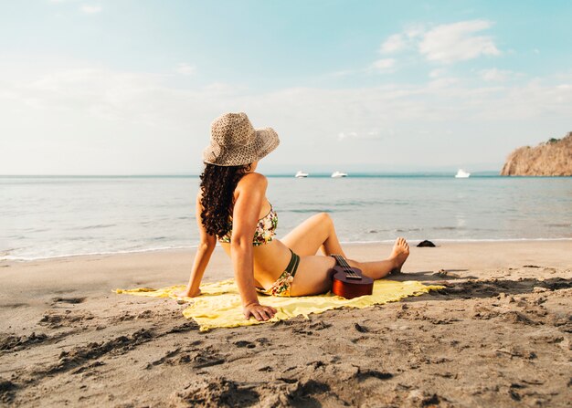 Vrouw in zwempak die met ukelele op strand zonnebaden