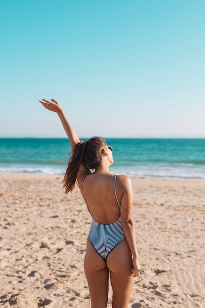 Gratis foto vrouw in zwempak golvende hand op kust