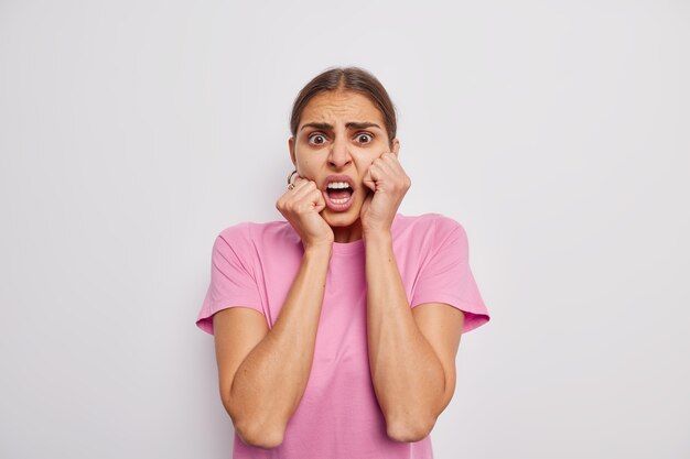 vrouw kijkt met een angstige, geschokte uitdrukking reageert op iets onaangenaams gekleed in een casual roze t-shirt op wit