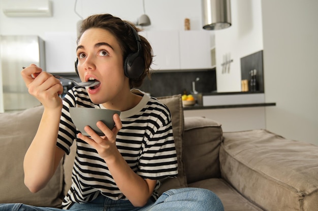 Vrouw kijkt met interesse naar de tv, staart naar het scherm en eet ontbijtgranen voor het ontbijt.