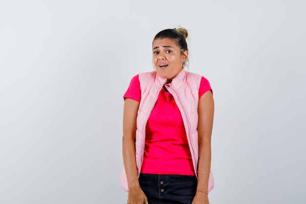 Vrouw kijkt naar camera in t-shirt, vest en kijkt beschaamd