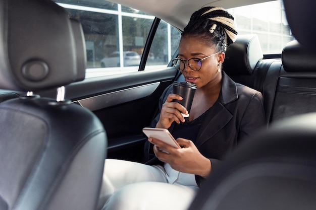Vrouw kijkt naar smartphone en heeft koffie in haar auto