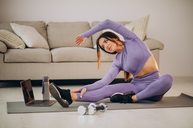 Vrouw kijkt naar tutorials en traint vanuit huis op mat met springtouw en dumbbells