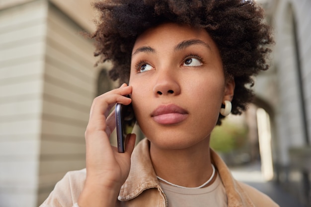 vrouw kijkt weg telefoneert via internationale verbinding nonchalant gekleed heeft mobieltje poseert buitenshuis