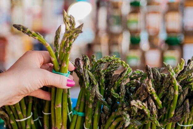 Vrouw koopt asperges. Bos verse asperges met vrouwelijke handen. Vrouw die asperges in close-up toont. Gezond eten concept