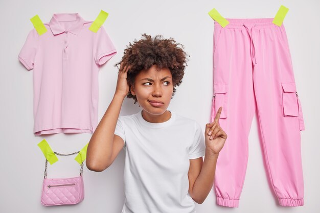 vrouw krabt hoofdpunten naar hangende broek bedenkt wat ze moet dragen vraagt je advies gekleed in een casual t-shirt op wit