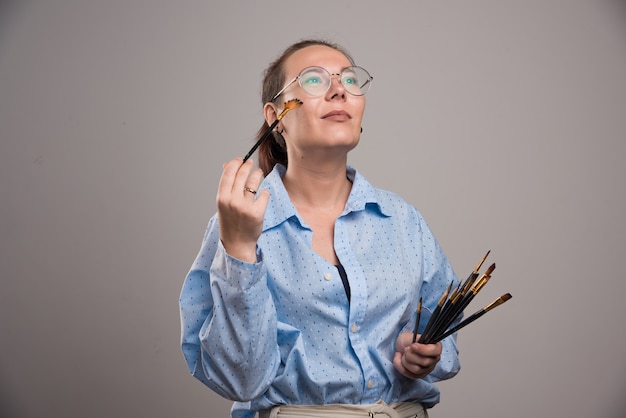 Vrouw kunstenaar houdt schilderij borstels in de buurt van haar gezicht op grijze achtergrond