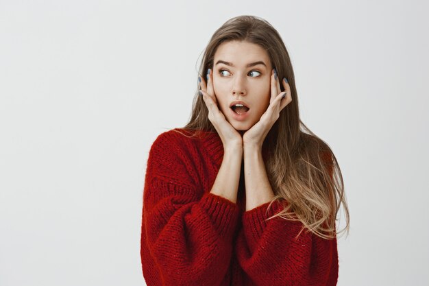 Vrouw kwam schokkend nieuws te weten en wilde het iemand vertellen. Portret van knap Kaukasisch vrouwelijk meisje, bezorgd en depressief gevoel, opzij kijkend met neergelaten kaak, hand in hand op gezicht, opgewonden