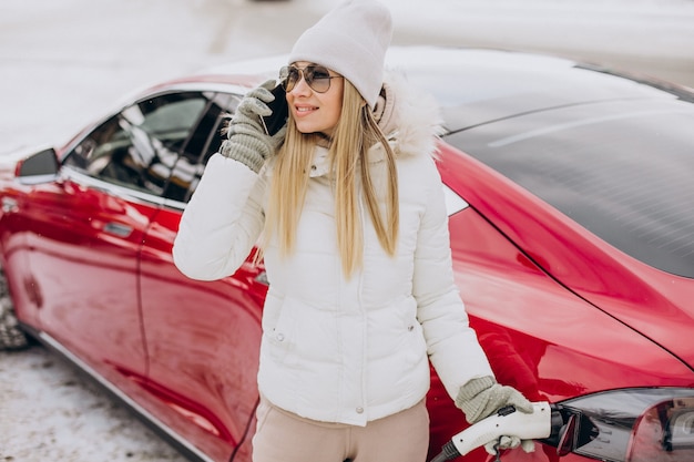 Vrouw laadt rode elektrische auto op, in de winter