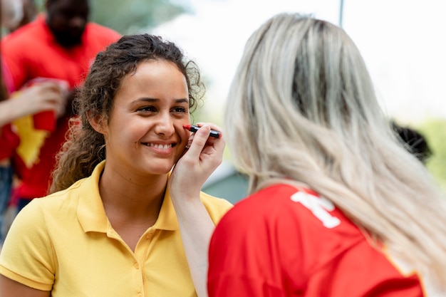 Vrouw laat haar wangen schilderen met de kleuren van haar team