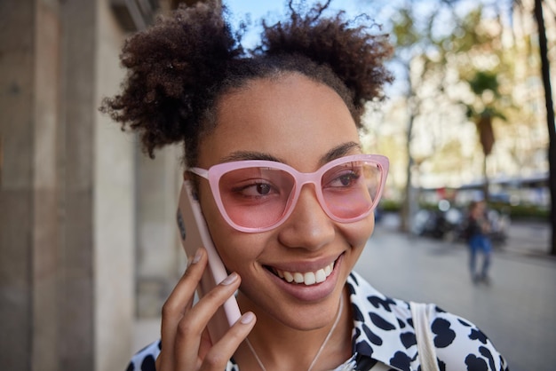 vrouw lacht breed toont witte tanden telefoneert via smartphone poseert tijdens straatgesprekken met vriend. Mensen en communicatieconcept