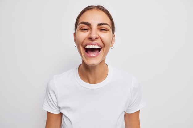 vrouw lacht oprecht drukt positieve emoties uit gekleed in casual t-shirt op wit glimlacht tandjes heeft een schone gezonde huid dwaasheden rond grinnikt naar de camera