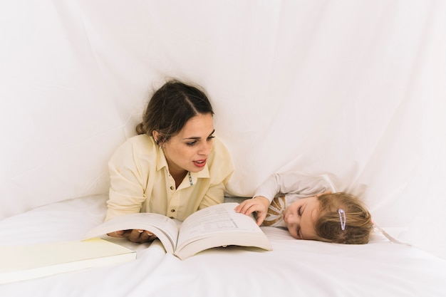 Gratis foto vrouw leesboek aan slapende dochter