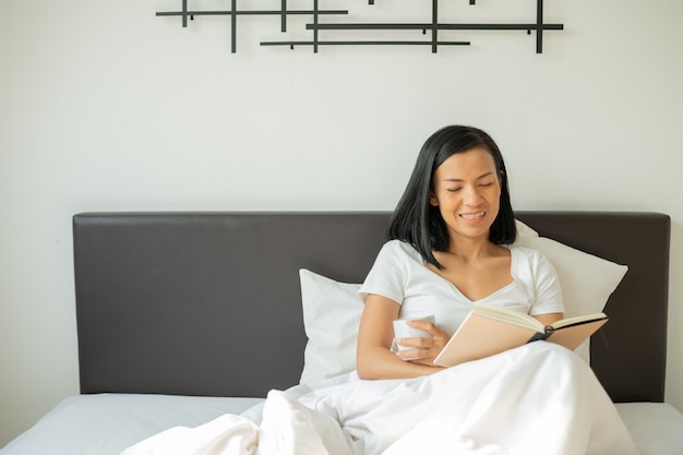 Vrouw leesboek met kopje koffie thuis in de slaapkamer.