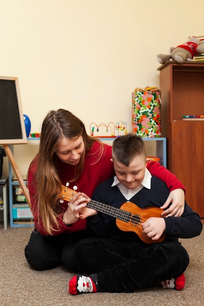 Vrouw lesgeven jongen met down syndroom om gitaar te spelen