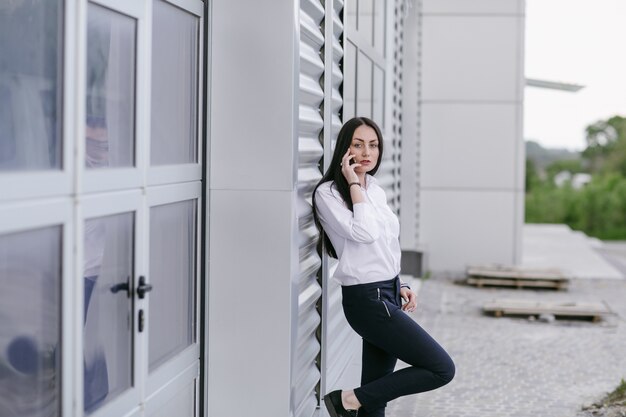 Vrouw leunend op een witte muur te praten over een mobiele telefoon