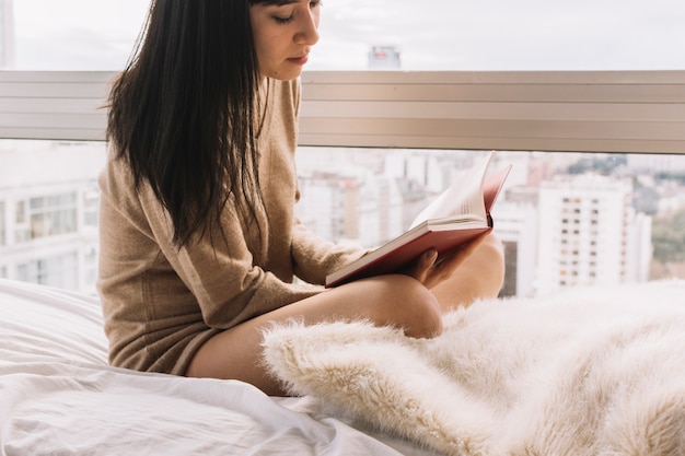 Gratis foto vrouw lezen in de buurt van venster bijsnijden