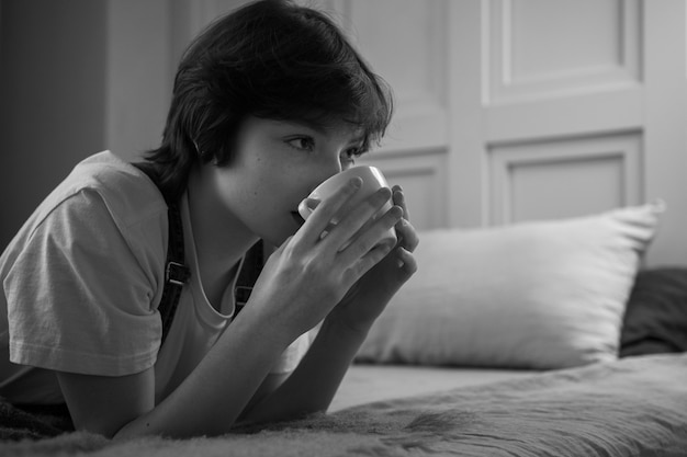 Vrouw liggend in bed met koffiekopje zijaanzicht