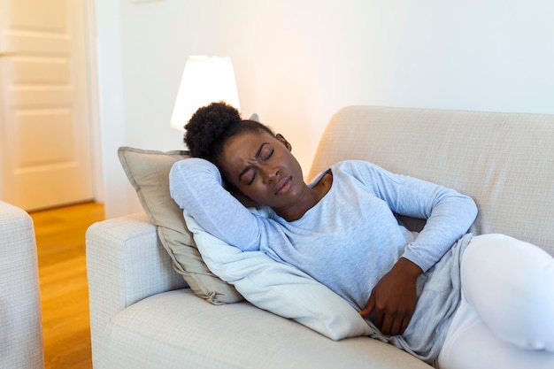 Vrouw liggend op de bank ziet er ziek uit in de woonkamer Mooie jonge vrouw liggend op bed en hand in hand op haar buik Vrouw met pijnlijke buikpijn op bed Menstruatie