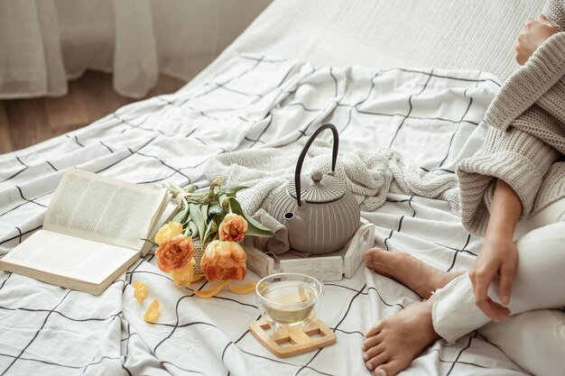 Vrouw ligt in bed met thee, een boek en een boeket tulpen